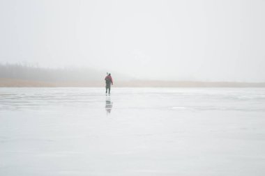 Novopskov, Ukrayna - 2 Ocak 2021: Kışın elinde matkapla gölette bir balıkçı balık tutacak. Kırsalda kış balıkçılığı. Yüzeyde, buz biraz erimiş, arka planda ağaçlar.