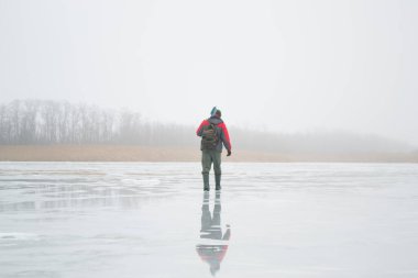 Novopskov, Ukrayna - 2 Ocak 2021: Bir balıkçı kışın elinde matkapla havuzda. Sisli bir sabahta kırsalda kış balıkçılığı. Ahenk ve barış kavramı. Balıkçı kameraya arkasını döndü ve uzaklaştı.