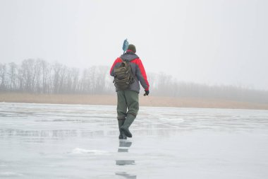 Novopskov, Ukrayna - 2 Ocak 2021: Bir balıkçı kışın elinde matkapla havuzda. Sisli bir sabahta kırsalda kış balıkçılığı. Ahenk ve barış kavramı. Balıkçı kameraya arkasını döndü ve uzaklaştı.