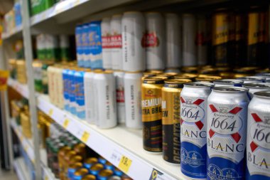 Ukrayna, Dnipropetrovsk. 05.06.2021 Aydınlatılmış vitrin, geniş bir bira çeşidiyle. Alkol gösterisi arka planı bulanıklaştırdı. Süpermarkette rafta. Renkli metal teneke kutular ve dükkanda bira.