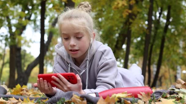 Блондинка дев'ятнадцять дівчат використовує смартфон на відкритому повітрі в осінньому парку або листяному лісі . — стокове відео