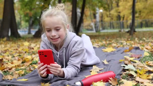 Blonda adolescenta fata folosind smartphone-ul în aer liber în parc toamna sau frunze pădure . — Videoclip de stoc