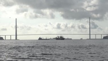 Köprünün altında gemiler var. Kablolu yayında kocaman bir köprü. Siluette bir sürü damar var. Tek renkli olsun. Sudan görüntüle