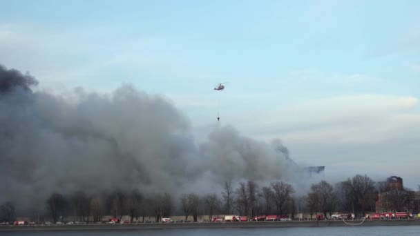 L'elicottero spegne il fuoco. Acqua dal secchio dei bambi. Fumo. Autocarri antincendio. — Video Stock