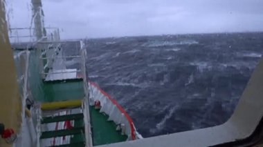 Fırtınada bir gemi. Bir sürü sıçrama. Köprüden görüntü. Gemi dalgalara tırmanıyor. İyi atıştı. Yüksek dalgalar gemiyi vurur. Suda beyaz köpük. Çok güçlü bir fırtına. Pruva dalgaları keser