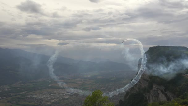 Kunstflug. Airshow. Doppeldecker. Flugzeug fliegt zwischen Bergen über Ebene. Rauch hinter dem Licht - Motorflugzeug Stock-Filmmaterial
