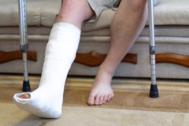 Adam alçılı bir kanepede oturuyor. Koltuk değnekleri yakında.