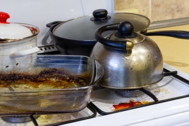 Kirli gaz ocağı. Pişirdikten sonra fırın. Mutfakta bir karışıklık var. Kirli su ısıtıcısı, tencere, cam fırın tabağı.