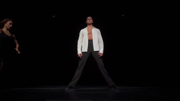 Les danseurs de salon couple sur scène sombre, partie de performance de danse.Femme en robe transparente noire courte court devant l'homme debout en chemise blanche déboutonnée, sauter, il l'attrape en vol et tient — Video