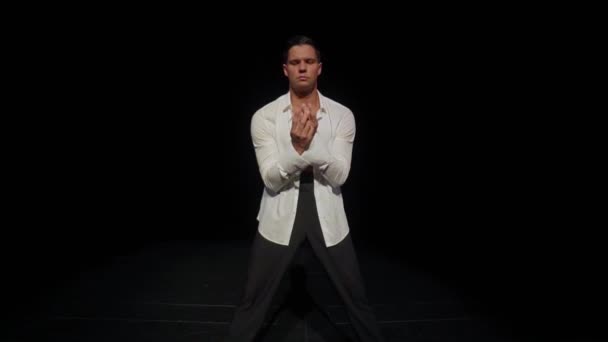 Joven bailarín de salón masculino con pecho desnudo, músculos pectorales fuertes, abdominales, con camisa blanca abierta, pantalones negros sobre fondo oscuro, expresando pasión. Danza en solitario y búsqueda del concepto de pareja de baile, punto medio.. — Vídeos de Stock