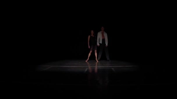 Bailarines de salón par sincrónicamente vienen en el escenario de darkness.Slow pasos flexibles hacia adelante y hacia los lados, girando y bailando, mujer en primer plano como una flor abierta, el hombre se inclina sobre su cara en la pasión. — Vídeo de stock