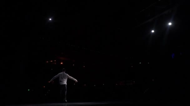 Solo performance fragment, ballroom danser op het podium in wit shirt, naakt gebruinde torso.View van podium naar donkere hal, achterste vlek lichten.Bewegend over, het maken van stappen, jupms, lunges, kettingen tours.Far afstand — Stockvideo