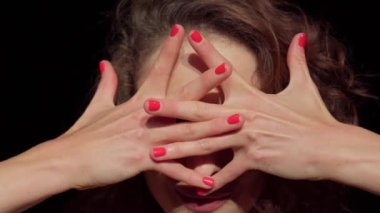 Yakından genç bir aktris, sahne makyajı, yüzünü çapraz parmaklarla, kırmızı tırnaklarla kaplıyor, hafif bir gülümsemeyle elleri yüzünüzden ayırıyor, başını arkaya atıyor, esnek bir boyun gösteriyor, kameraya bakıyor. Dalgalı kahverengi saçlar..