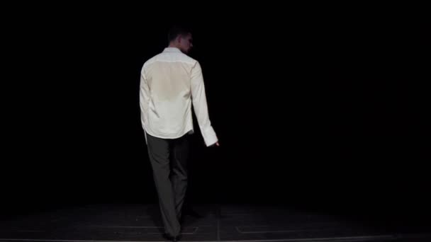 Male ballroom dancer walk off into darkness of stage with slow dance gait,holding his right hand as if someones hand,in white unbuttoned shirt,black trousers,patent leather shoes,rear view.Copy space — Stock Video