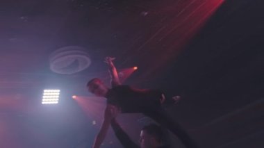 Artistik patinajcılar buz pateni sahasında yan destekte kaldırma, kollar ve bacaklar gerilmiş, eksen etrafında yavaş çekim, neon projektöründe köşegen çekim yapıyorlar. Prova.