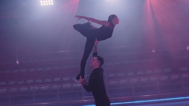 El par de patinadores de la figura realiza un elevador aéreo complejo, el hombre sostiene a la mujer con el brazo doblado por el patín, apoyándola por la cintura con el brazo enderezado, la mujer sosteniendo el agarre cruzado, girando alrededor.. — Vídeos de Stock