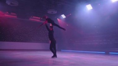 Artistik patinajcılar buz pateni pistinde yan destekte kaldırma hareketi yapıyorlar, kollar ve bacaklar gerilmiş, eksen etrafında dönüyorlar, neon ışıkları altında çapraz çekim yapıyorlar. Prova.