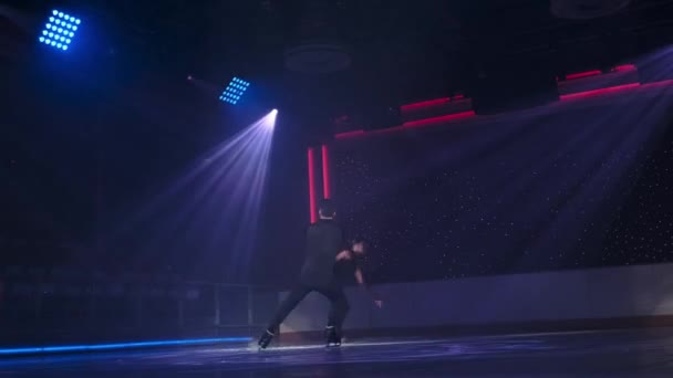 La paire de patineurs artistiques effectue une portance rotative stationnaire sous les projecteurs. L'homme tient la femme par les deux chevilles avec les bras croisés, tournant, elle plane sur la glace avec les bras redressés le long du corps. Répétition — Video