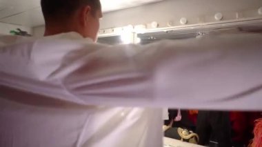 Gösteriden önce soyunma odasında giyinen genç yakışıklı bir adam, bronzlaşmış gövdenin çıplak belinde, boynunda kolyesi, beyaz gömlek giyiyor, aynanın önünde dikiliyor ve yansımasına bakıyor..