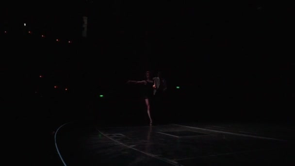 Dois dançarinos de salão saindo da escuridão para o palco iluminado com passos flexíveis, balanços de mão, rotações de quadril no estilo de dança latino-americano, o homem transforma a mulher em salto mortal, ela senta-se em profunda lunge. — Vídeo de Stock