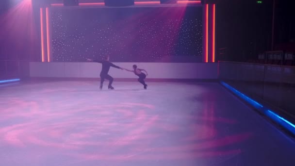 Paire de patineurs artistiques tournant sur la patinoire, la femme entre dans la spirale de la mort, plane dans l'air parallèlement à la glace, l'homme tient ses mains. Élévation de patinage artistique, ralenti, balançoire de la caméra en diagonale, prise de vue lointaine — Video