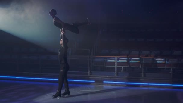 Paire de patineurs artistiques sur patinoire effectuant un levage aérien, l'homme tient la femme dans une prise main-hanche, se déplaçant lentement de droite à gauche, la jambe pliée au genou.. — Video