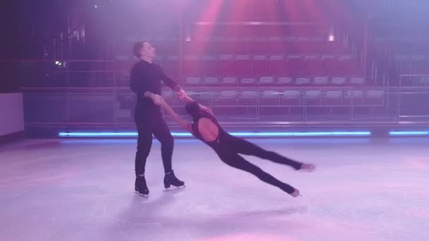 Pair of figure skaters in black stage costumes perform death spiral element,partner releases woman,they skate in synchronous parallel step movements.Slow motion.Concept of pair skating,ice dancing — ストック動画
