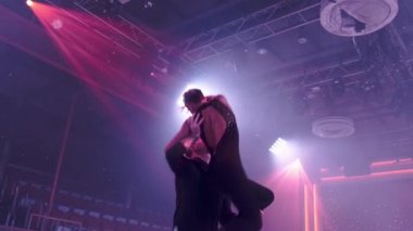 Siyah sahne kostümlü iki artistik patinajcı boş salonda sahne ışıklarını destekliyor. Yavaş çekimde yakın çekim. Artistik patinaj okulu, eğitim ve gösteri veya yarışma hazırlığı kavramı.