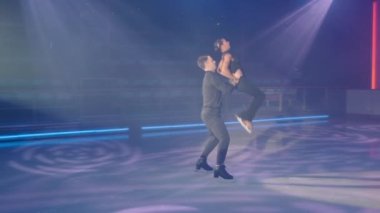 Artistik patinajcı geriye doğru hareket ediyor kadın partneri belinden kaldırıyor, fırlatıyor, yukarıdan atlamaya yardım ediyor, kadın buzun üzerine düşüyor. Kayak yaparken karmaşık figürler. Çok yavaş çekim tam HD .