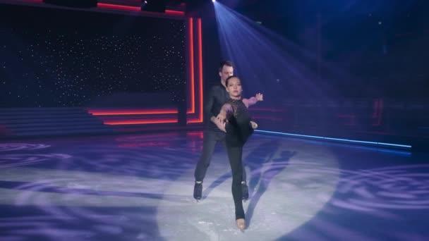 Female figure skater moves to camera in arabesque,beautifully stretching arm forward and making graceful movements with her hand,man moves behind her,stops her by leg and pulls her back.Slow motion. — Stock Video