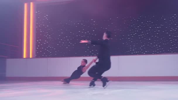 Pair of figure skaters rotating on ice rink,woman goes into death spiral,hovers in air parallel to ice her legs in split, man holds her by hands. Figure skating lift,slow motion support,distant shot. — Stock Video