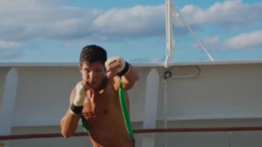 Strong young man with naked torso does box workout and shadow boxing with resistance band training strap system 