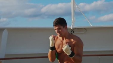 Çıplak gövdeli çekici genç adam boks yapıyor ve direnç bandı eğitim sistemiyle gölge boksu yapıyor.