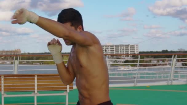 Молодой сильный привлекательный мускулистый мужчина с обнаженным туловищем, тренирующийся в теневом боксе на вертолетной площадке круизного лайнера — стоковое видео