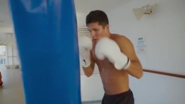 Attractive strong man with beautiful body naked torso kicks punching bag on open ship deck