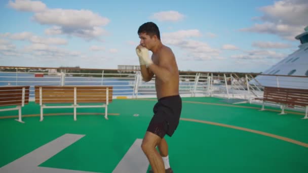 Atractivo hombre patadas golpes rápidos ejercicio sombra boxeo en helipuerto a bordo de crucero — Vídeos de Stock