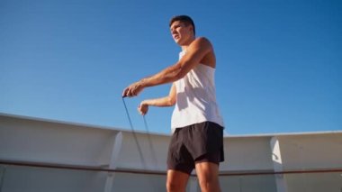 Beyaz tişörtlü atletik genç adam halatla dışarıda zıplıyor.