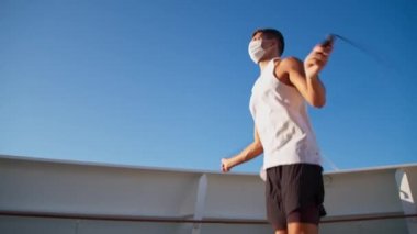 Handsome young athletic man in white mask and t-shirt jump rope outdoor