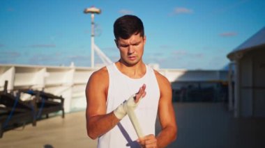 Athletic attractive man puts on hands wraps to do box outside onboard cruise ship
