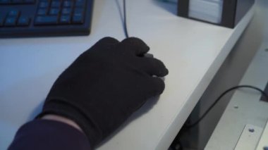 Close-up of hand of production process operator, holding and moving wired computer mouse in black work gloves. Concept of management and quality control.Blurred keyboard behind on white table surface 