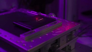 Laser engraving process camera passing by horizontally,working platform of laser machine with object for engraving lighted by in changing light color of LED source, side view. Ray movement on surface.