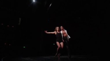 Sahnede dans eden kadın ve erkek. Salon dansı, oditoryumun yan görüntüsü. Ön plandaki kadın dansçı takla atıyor, partner onu omuzlarının üzerine kaldırıyor. Yavaş çekim.