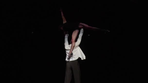 男人把女人抱在伸出的胳膊上 侧身提起 一条腿朝下 扭动着胳膊 舞者身穿黑色的白色舞衣 舞者在黑暗的舞台上赤身裸体 泛泛泛而谈 — 图库视频影像