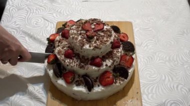 Yetişkin bir kadın, güzel bir kremalı pastayı büyük bir mutfak bıçağıyla çilekli dilimlerle bir ev mutfağında tahta bir kesme tahtasıyla keser. Tatil konsepti. Yakın plan. Yüzsüz. Üst Manzara. 4K.