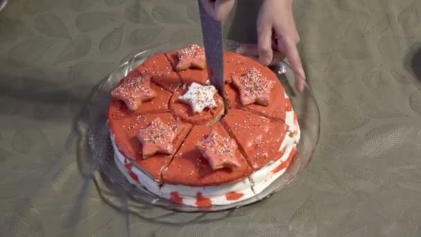 En vuxen kvinna omgiven av barn skär en vacker rund kaka dekorerad med röd glasyr i bitar med en stor kökskniv. Begreppet familjefest. Närbild. Ansiktslös. — Stockvideo