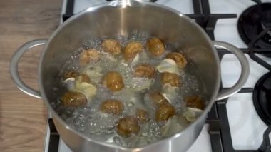 Erkek eli, ev mutfağındaki bir tencere kaynar suya salyangoz atıyor. Sağlıklı yemek pişirme kavramı. Avrupa mutfağı. İnsan yok. 4K.