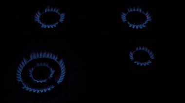 Dört gaz ocağı yanıyor ve karşılığında siyah bir arka planda mutfak sobası yanıp sönüyor. Enerji krizi kavramı. Gaz kaynaklarının yok edilmesi. Yakın plan. İnsanlar olmadan. Üst Manzara. 4K.