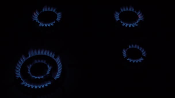 Vier gasbranders branden en gaan op hun beurt op een zwarte achtergrond op en neer op het fornuis. Het concept van de energiecrisis. Beëindiging van de gasvoorziening. Een close-up. Zonder mensen. Bovenaanzicht. 4K. — Stockvideo