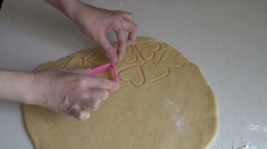 Bir kadın şenlikli kurabiyeler hazırlar ve çiğ hamurdan kalp şeklinde kuru sıkı parçalar çıkarır. Tatili hazırlama konsepti. Yemek pişirmek. Yüzsüz. Yakın plan. Üst Manzara. 4K