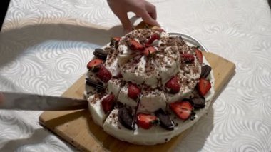 Güzel ev yapımı çilekli pastayı büyük bir mutfak bıçağıyla ahşap bir tahtada aynı parçalara ayıran kadın ellerine yakın plan. Ev tatili kavramı. Yüzsüz. Üst Manzara. 4K